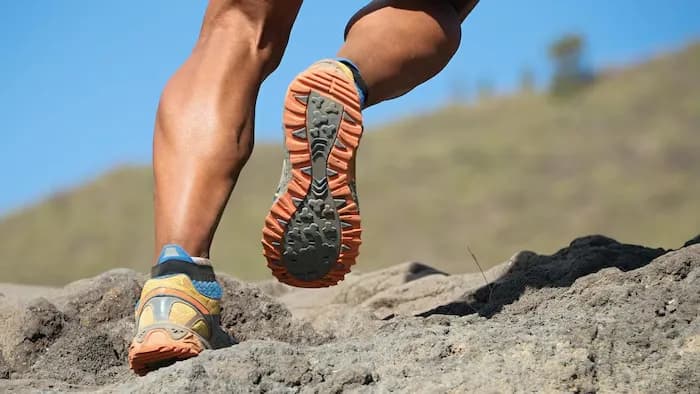 Jambes d’un coureur en chaussures de trail sur un sol rocheux